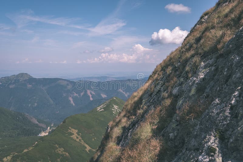 Skalnaté vrcholky hor s turistickými stezkami na podzim ve slovenských Tatrách v západních Karpatech s modrou oblohou a pozdní trávou na kopcích.