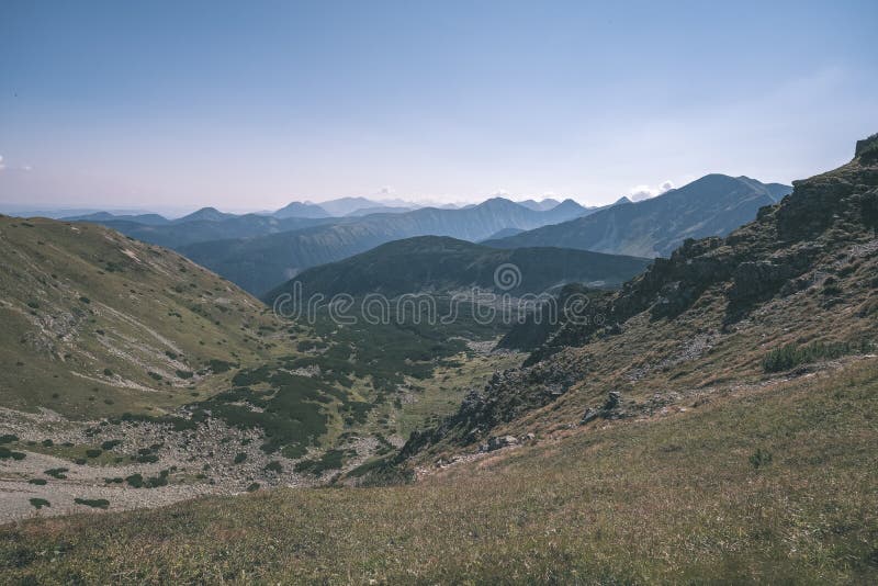 Skalnaté vrcholky hôr s turistickými chodníkmi na jeseň v slovenských Tatrách v západných Karpatoch s modrou oblohou a neskorou trávou na kopcoch.