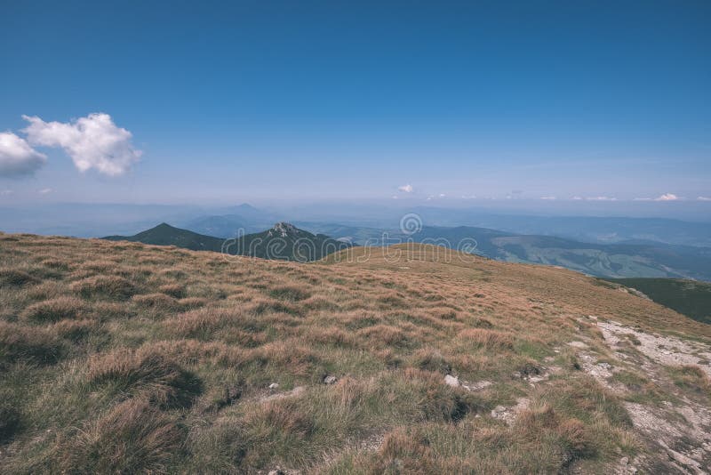 Skalnaté vrcholky hor s turistickými stezkami na podzim ve slovenských Tatrách v západních Karpatech s modrou oblohou a pozdní trávou na kopcích.