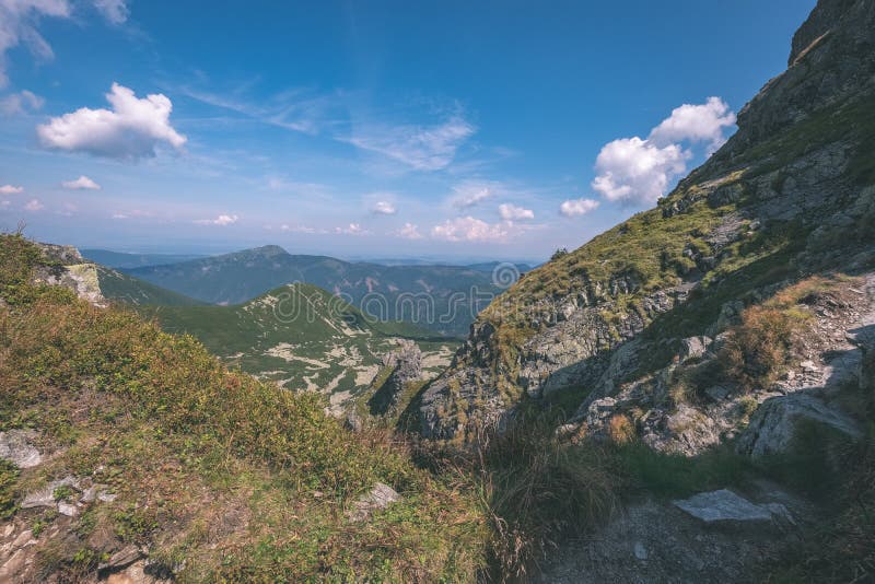 Skalnaté vrcholky hor s turistickými stezkami na podzim ve slovenských Tatrách v západních Karpatech s modrou oblohou a pozdní trávou na kopcích.