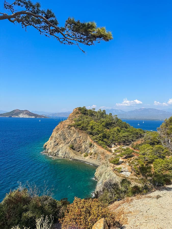 Coastal landscape, rocky promontory covered in greenery juts into a vibrant blue sea sailboats scatter the water, framed stock images