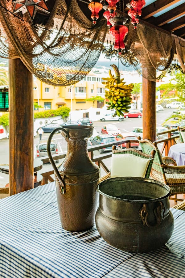 Rocznika dęciak i puszkujemy na stole z barwionym tablecloth Wisząca wiązka dojrzali banany i lokalna wioska w fotografia stock Rocznika dęciak i puszkujemy na stole z barwionym tablecloth Wisząca wiązka dojrzali banany i lokalna wioska w fotografia stock
