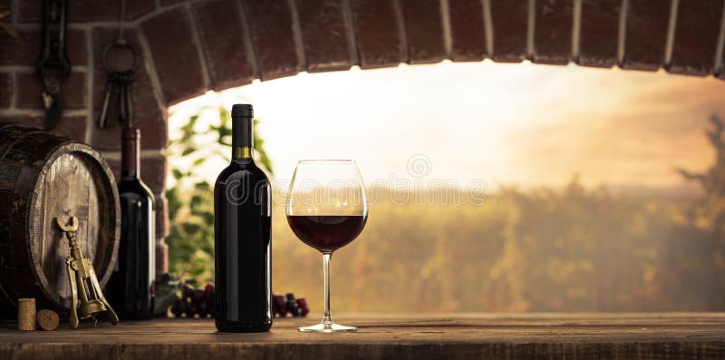 Red wine tasting in the wine cellar: wineglass and bottles next to the window and panoramic view of vineyards at sunset. Red wine tasting in the wine cellar: wineglass and bottles next to the window and panoramic view of vineyards at sunset