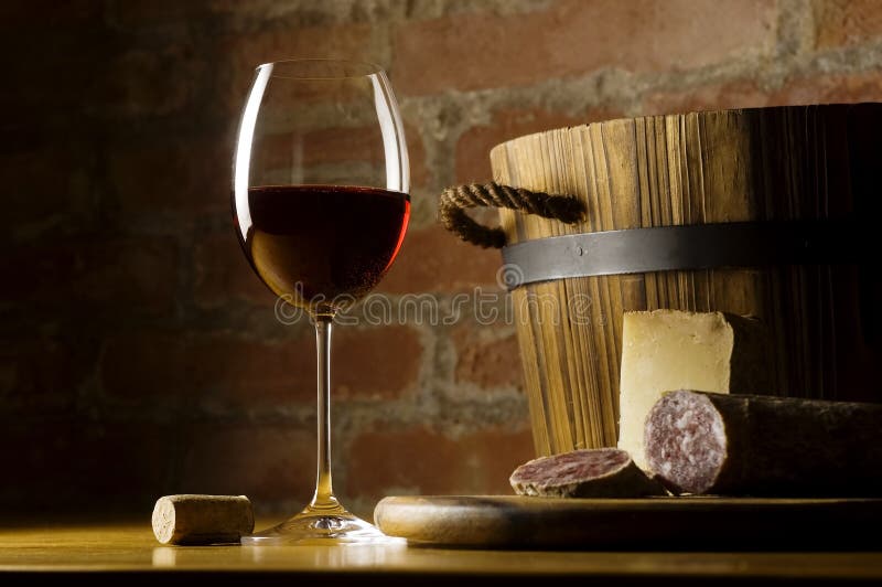 Cutting board with genuine Italian food in a rural kitchen. Red wine glass, ripe hard cheese from ewe's milk and sausage. Warm ray of light in the background. Cutting board with genuine Italian food in a rural kitchen. Red wine glass, ripe hard cheese from ewe's milk and sausage. Warm ray of light in the background.