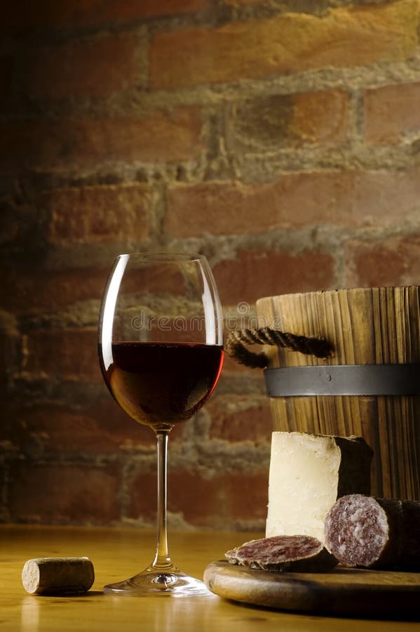 Cutting board with genuine Italian food in a rural kitchen. Red wine glass, ripe hard cheese from ewe's milk and sausage. Warm ray of light in the background. Space for text. Cutting board with genuine Italian food in a rural kitchen. Red wine glass, ripe hard cheese from ewe's milk and sausage. Warm ray of light in the background. Space for text