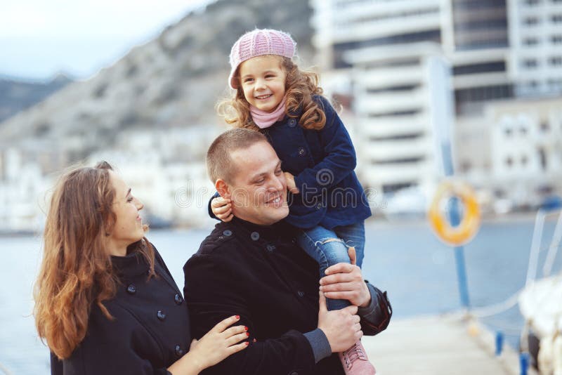 Portrait of happy young family walking with their child on berth near sea in the city, still life photo. Portrait of happy young family walking with their child on berth near sea in the city, still life photo