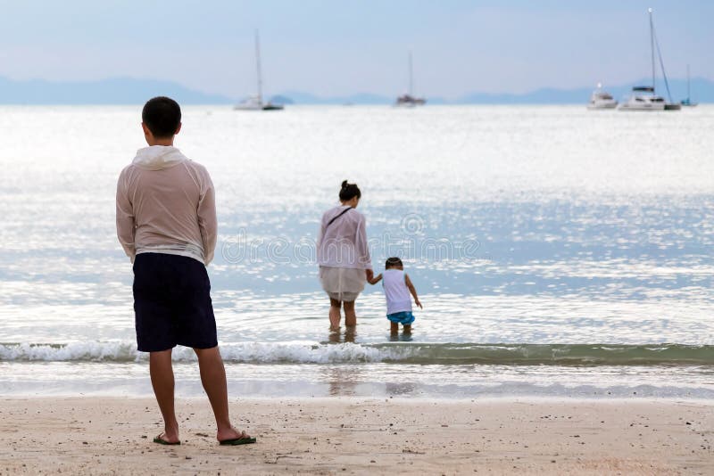 Rodzina na morzu Ojciec ogląda jego syna i żony wchodzić do wodę od piaskowatej plaży obrazy stock Rodzina na morzu Ojciec ogląda jego syna i żony wchodzić do wodę od piaskowatej plaży obrazy stock
