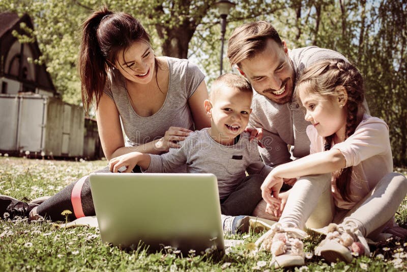 Happy family using laptop, sitting on the grass. Happy family using laptop, sitting on the grass.