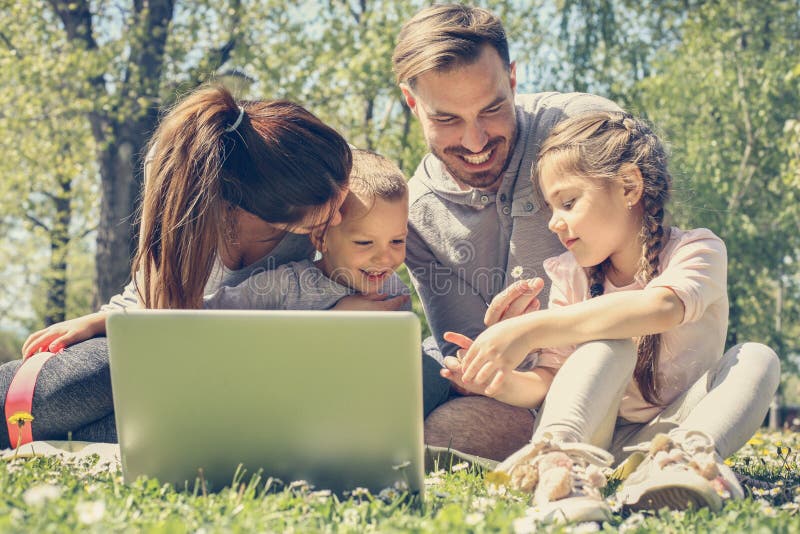 Happy family using laptop, sitting on the green grass. Happy family using laptop, sitting on the green grass.