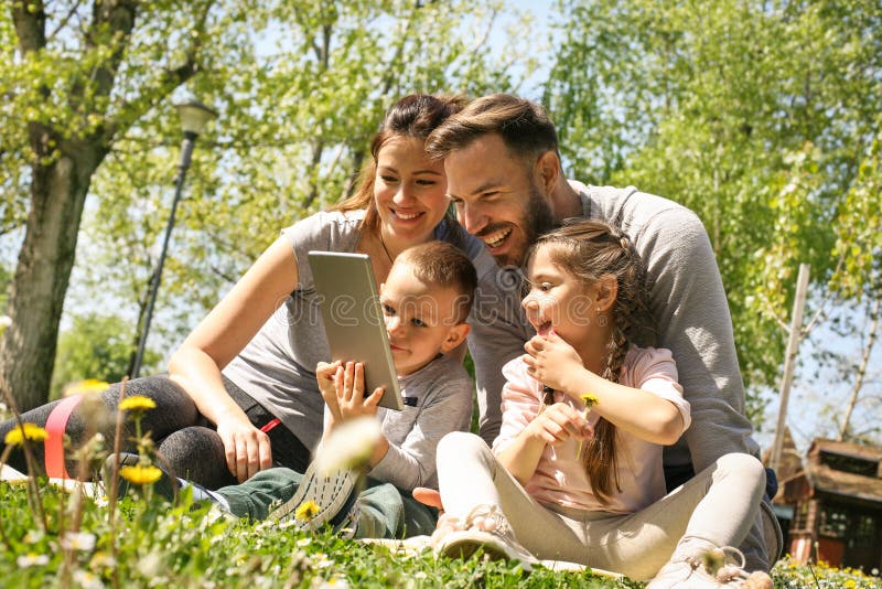 Happy family using tablet, sitting on the green grass. Happy family using tablet, sitting on the green grass.