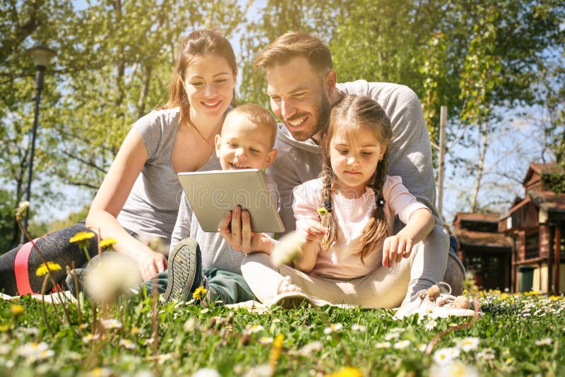 Happy family using tablet outdoors, sitting on the green grass. Happy family using tablet outdoors, sitting on the green grass.