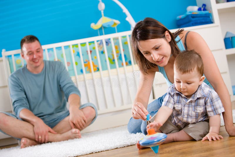 Portrait of happy family at home. Baby boy ( 1 year old ) and young parents father and mother sitting on floor and playing together at children's room, smiling. Portrait of happy family at home. Baby boy ( 1 year old ) and young parents father and mother sitting on floor and playing together at children's room, smiling.