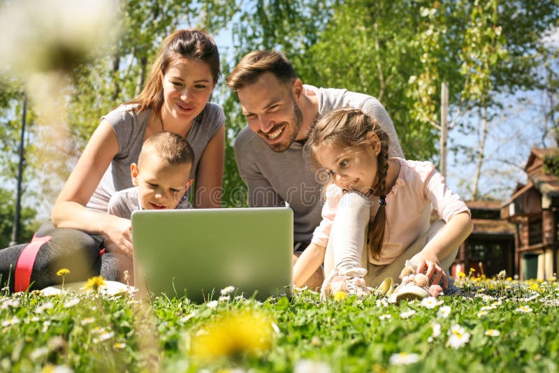 Happy family using laptop, sitting on the green grass. Happy family using laptop, sitting on the green grass.