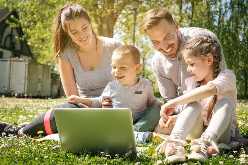 Happy family using laptop outdoors, sitting on the green grass. Happy family using laptop outdoors, sitting on the green grass.