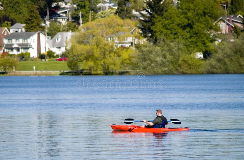 An adult male paddling a red boat in a lake. An adult male paddling a red boat in a lake.