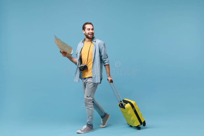 Cheerful traveler tourist man in yellow casual clothes with photo camera isolated on blue background. Male passenger traveling abroad on weekends. Air flight journey concept. Hold suitcase, city map. Cheerful traveler tourist man in yellow casual clothes with photo camera isolated on blue background. Male passenger traveling abroad on weekends. Air flight journey concept. Hold suitcase, city map