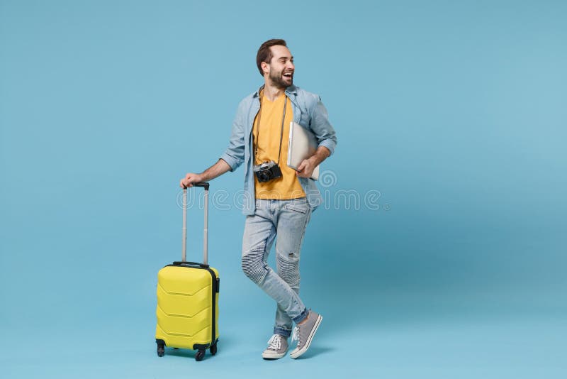 Cheerful traveler tourist man in yellow clothes with photo camera isolated on blue background. Male passenger traveling abroad on weekend. Air flight journey concept. Hold suitcase laptop pc computer. Cheerful traveler tourist man in yellow clothes with photo camera isolated on blue background. Male passenger traveling abroad on weekend. Air flight journey concept. Hold suitcase laptop pc computer