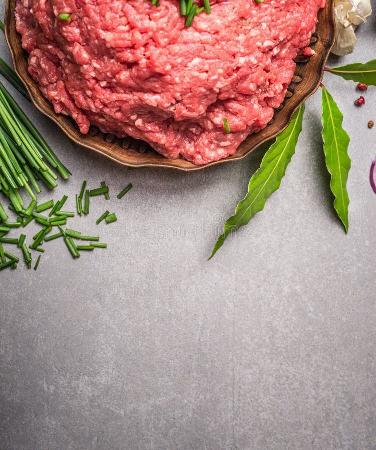 Rohes Kraftfleisch und frische grüne Gewürzbestandteile für das geschmackvolle Kochen auf Steinhintergrund lizenzfreie stockbilder Rohes Kraftfleisch und frische grüne Gewürzbestandteile für das geschmackvolle Kochen auf Steinhintergrund lizenzfreie stockbilder