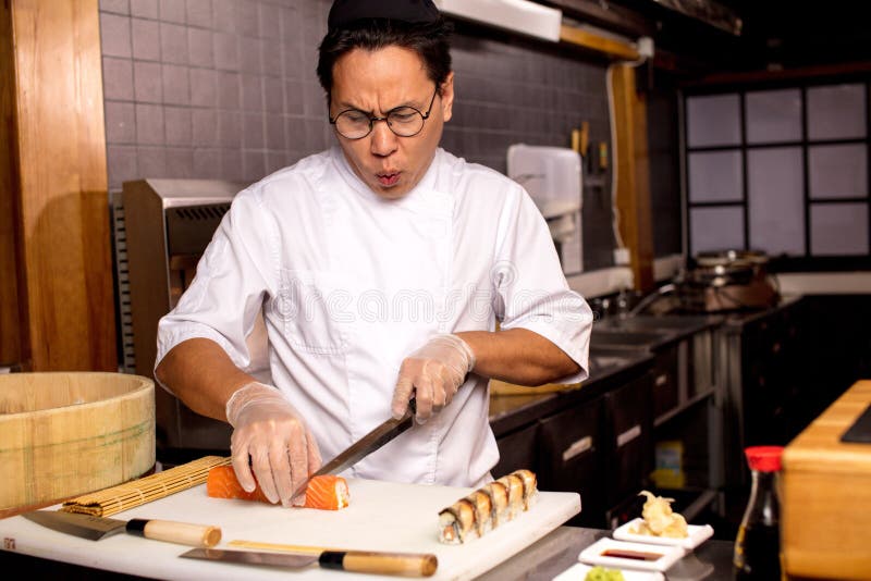Rolig asiatisk kock som sjunger sånger, medan förbereda sushi arkivbild Rolig asiatisk kock som sjunger sånger, medan förbereda sushi arkivbild