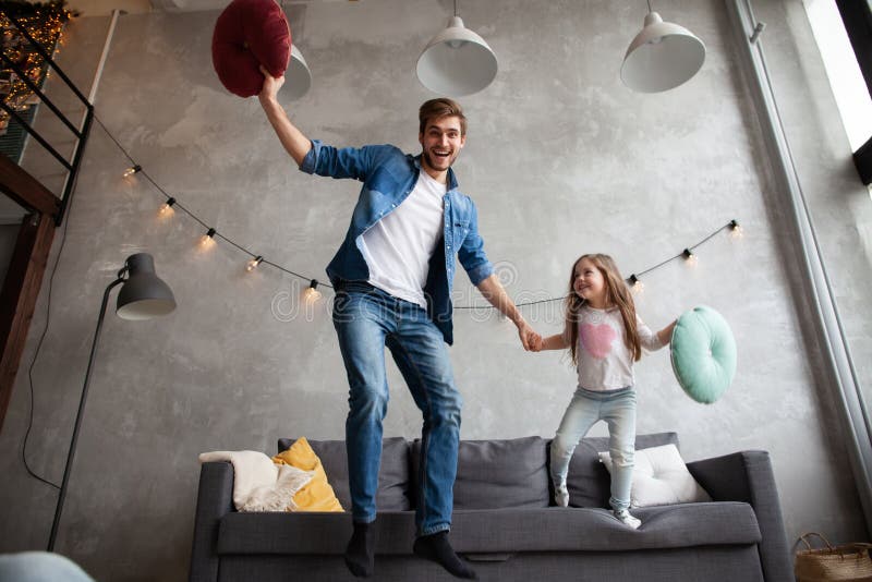 Rolig fader och gullig ungedotter som skrattar banhoppningen som har gyckel i vardagsrum, aktiv familj som tycker om rörande spel royaltyfria foton Rolig fader och gullig ungedotter som skrattar banhoppningen som har gyckel i vardagsrum, aktiv familj som tycker om rörande spel royaltyfria foton