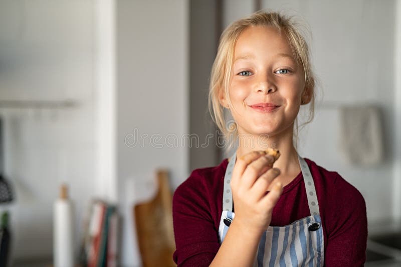 Funny little girl eating handmade cookie and looking at camera. Beautiful smart child holding a freshly baked biscuit. Little girl eating a chocolate cookie and looking with a funny expression. Funny little girl eating handmade cookie and looking at camera. Beautiful smart child holding a freshly baked biscuit. Little girl eating a chocolate cookie and looking with a funny expression