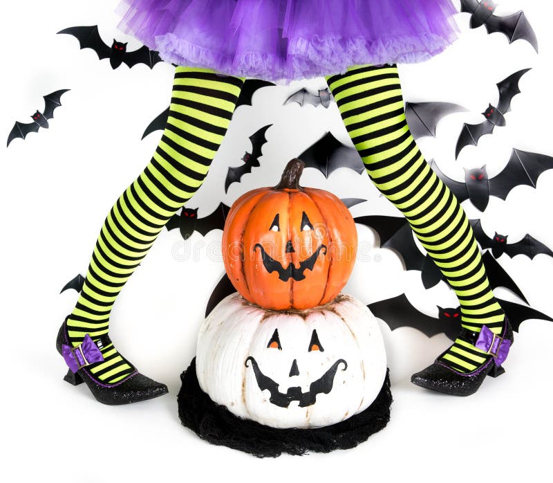Rolig gräsplansvart gjorde randig ben av lite flickan med den halloween dräkten av en häxa med häxaskor och smileyhalloween pumpa arkivbild Rolig gräsplansvart gjorde randig ben av lite flickan med den halloween dräkten av en häxa med häxaskor och smileyhalloween pumpa arkivbild