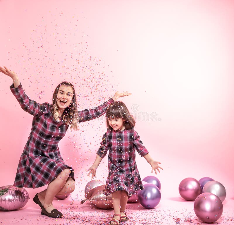 Rolig mamma och barn p? en rosa bakgrund Liten flicka och moder som har gyckel med ballonger och konfettier royaltyfri bild Rolig mamma och barn p? en rosa bakgrund Liten flicka och moder som har gyckel med ballonger och konfettier royaltyfri bild