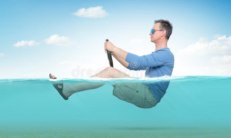 Rolig man i solglasögon, kortslutningar, T-tröja och sandalritter på havet med ett bilstyrninghjul Begrepp av att g? p? semester royaltyfria bilder Rolig man i solglasögon, kortslutningar, T-tröja och sandalritter på havet med ett bilstyrninghjul Begrepp av att g? p? semester royaltyfria bilder