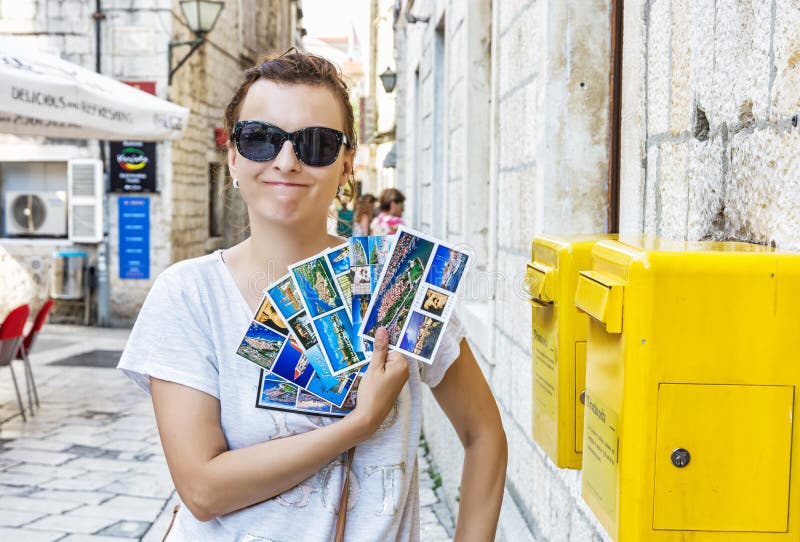 Rolig turist- kvinna med den near gula stolpeasken för postcarsd i Trogi royaltyfri bild Rolig turist- kvinna med den near gula stolpeasken för postcarsd i Trogi royaltyfri bild