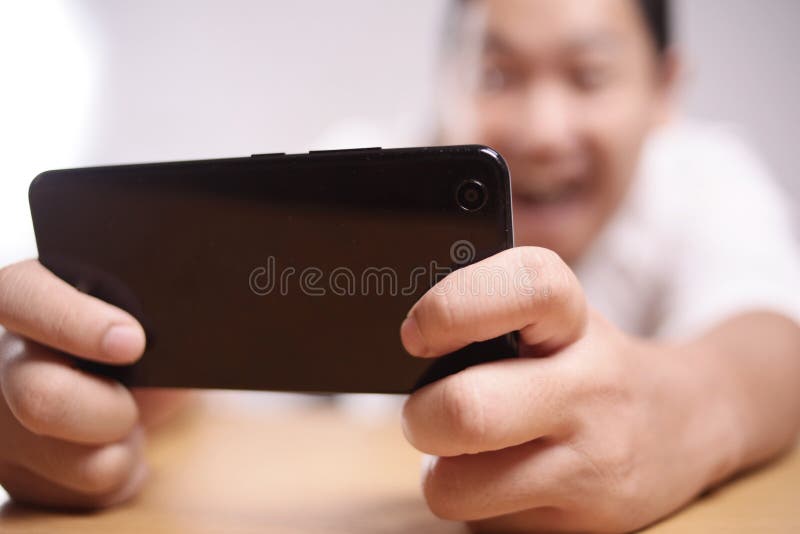 Rolig ung asiat Guy Playing Games p? den smarta telefonen f?r minnestavla arkivbilder Rolig ung asiat Guy Playing Games p? den smarta telefonen f?r minnestavla arkivbilder