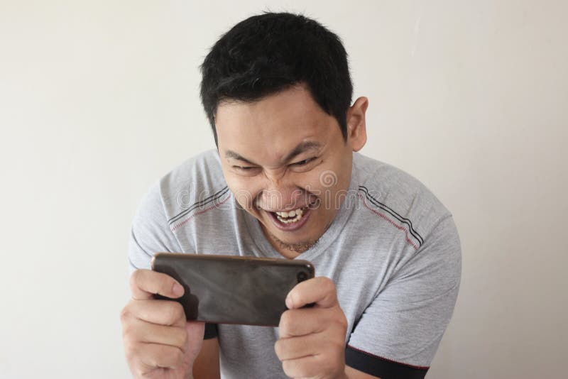 Rolig ung asiat Guy Playing Games på den smarta telefonen för minnestavla arkivfoton Rolig ung asiat Guy Playing Games på den smarta telefonen för minnestavla arkivfoton