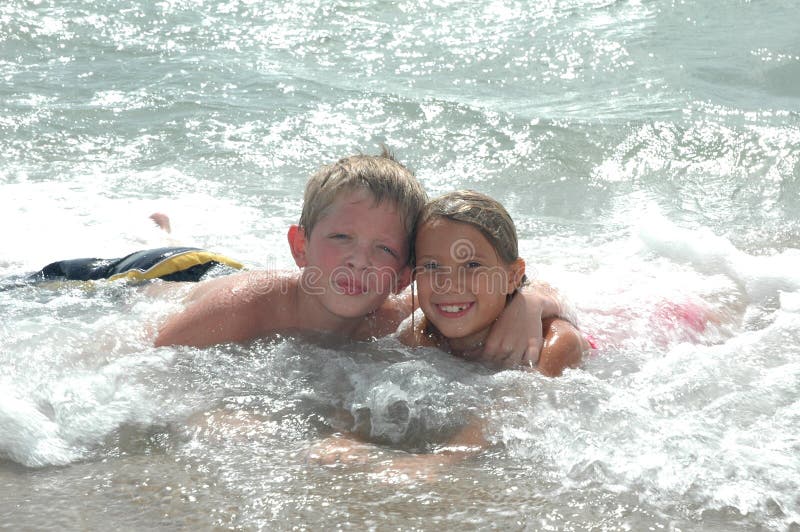 Happy Cousins hang together on vacation on the beach. Boy and girl laying in the ocean waves looking at the camera. Happy Cousins hang together on vacation on the beach. Boy and girl laying in the ocean waves looking at the camera.