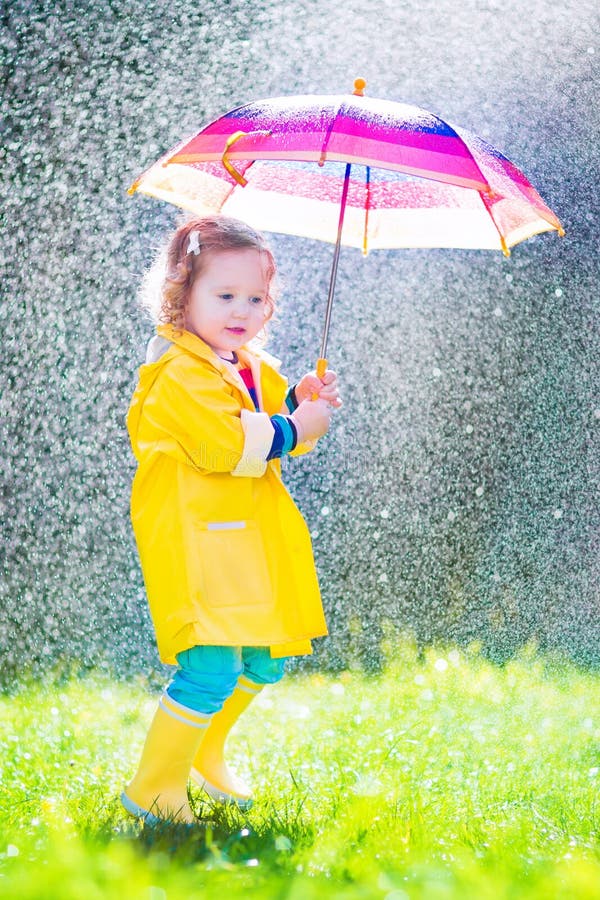 Roligt litet barn med paraplyet som spelar i regnet