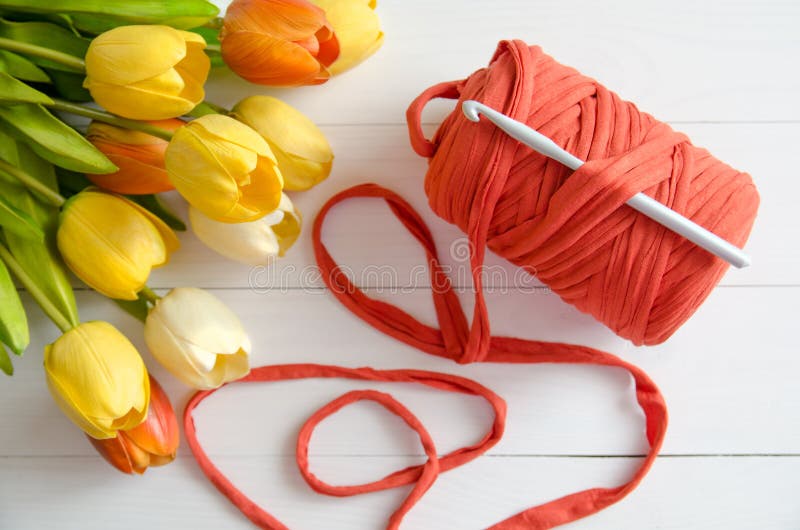 Roll of cotton yarn and a crochet hook with a bouquet of orange and yellow tulips on white wooden background. stock image Roll of cotton yarn and a crochet hook with a bouquet of orange and yellow tulips on white wooden background. stock image