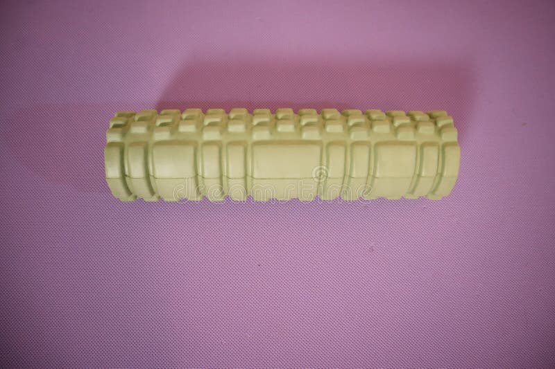 Green foam roller lying on its side on a vibrant purple background, with empty space for text. Minimalist fitness and recovery concept.