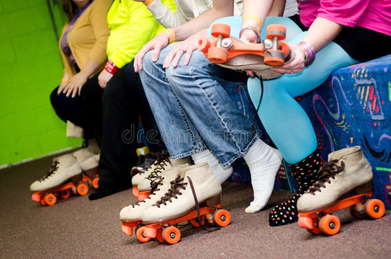 A row of Roller Skaters prepare for skating by putting their feet into skates. A row of Roller Skaters prepare for skating by putting their feet into skates