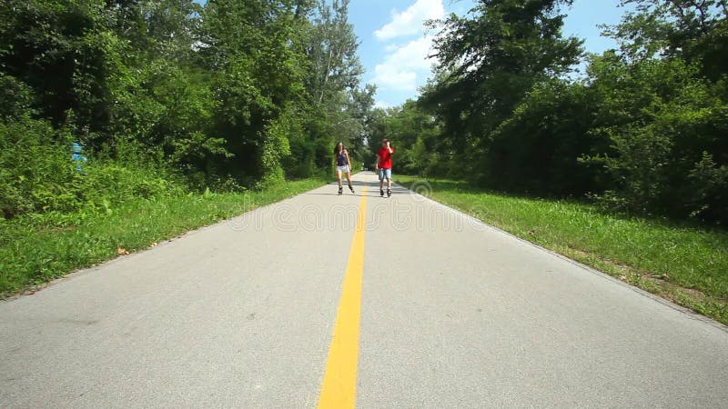 Rollerbladers ζεύγους που κάνουν πατινάζ προς τη κάμερα στο πάρκο