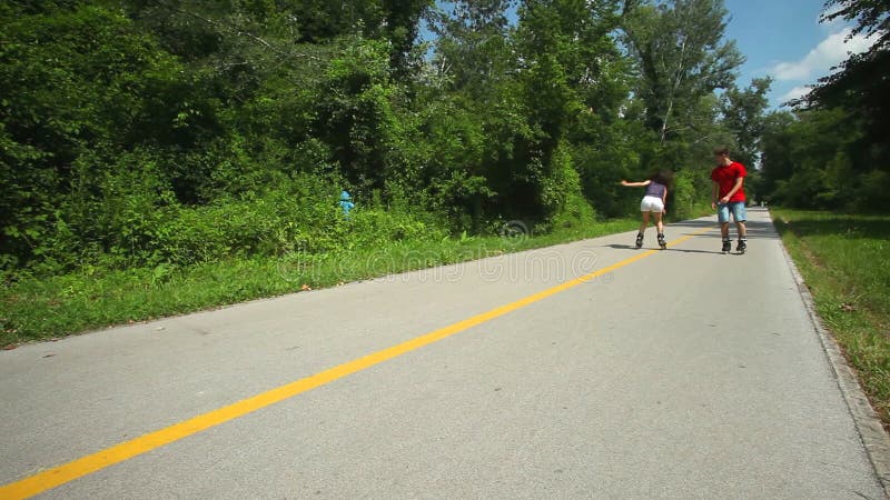 Rollerbladers ζεύγους που κάνουν πατινάζ προς τη κάμερα στο πάρκο