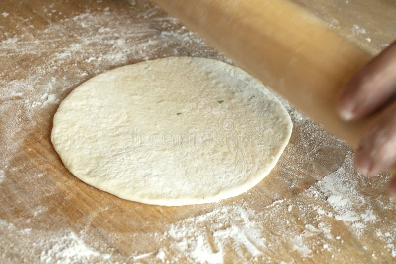 Rolling out the dough with a rolling pin on a cutting board to make homemade Naan bread. Rolling out the dough with a rolling pin on a cutting board to make homemade Naan bread