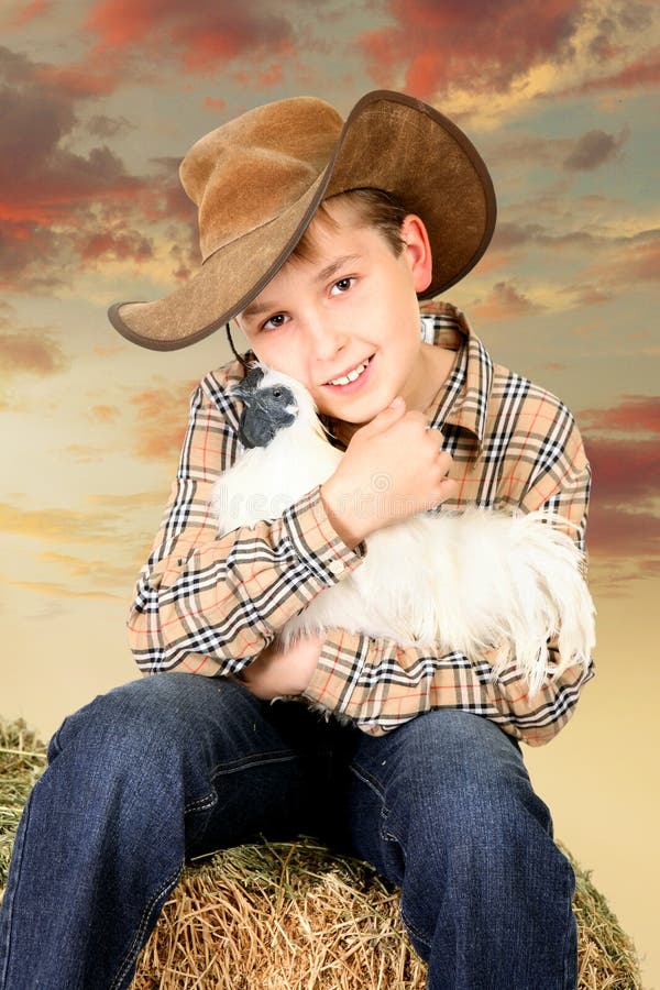 Rolnej chłopiec obsiadanie na beli trzyma kurczaka siano