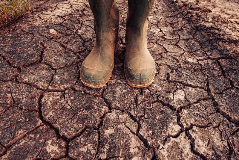 Rolnik stoi na suchej ziemi ziemi w gumowych butach