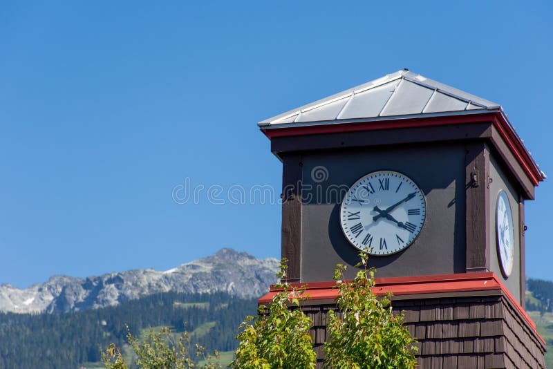 Roman Numeral Clock Tower with rocky mountains and blue sky in the background stock image