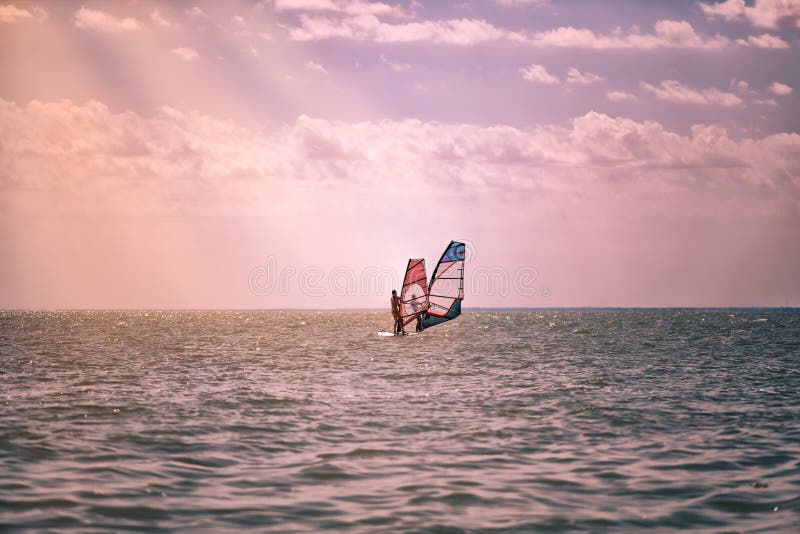 Romance en el hombre y la mujer de los pares del mar junto que navegan en un tablero del windsurf mientras que de vacaciones en e fotografía de archivo Romance en el hombre y la mujer de los pares del mar junto que navegan en un tablero del windsurf mientras que de vacaciones en e fotografía de archivo
