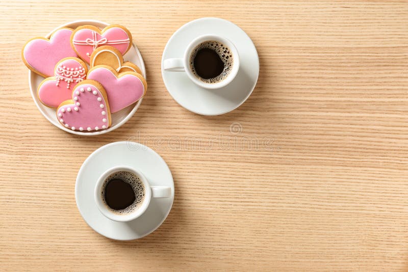 Romantic breakfast with heart shaped cookies and cups of coffee on wooden table, top view.