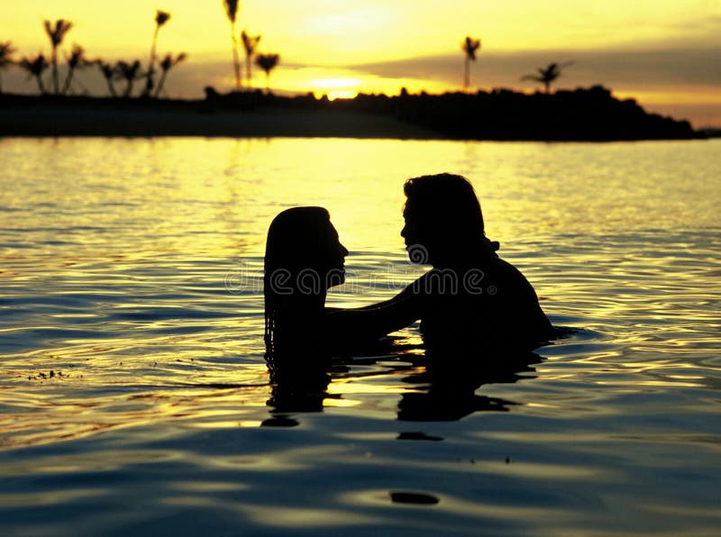 Masculino a una mujer ella abrazó en el agua sobre el atardecer.