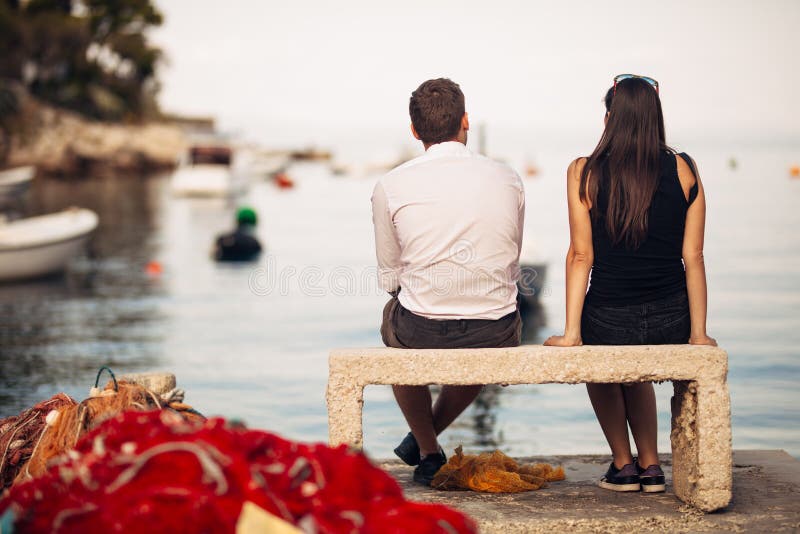 Romantic couple on a date in nature,sitting on the bench looking at serene ocean scene.People living on the coast lifestyle