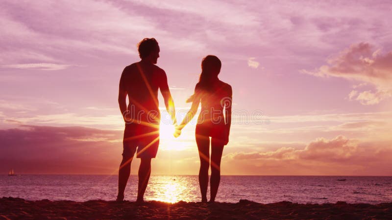 Romantic couple holding hands on beach at sunset with amazing light and colors. Young fit couple on honeymoon enjoying travel vacation summer holidays on beach