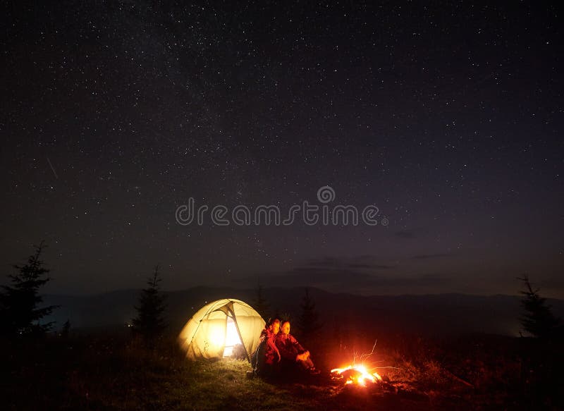 Young couple hikers resting near illuminated tent, camping in mountains at night under starry sky royalty free stock image Young couple hikers resting near illuminated tent, camping in mountains at night under starry sky royalty free stock image