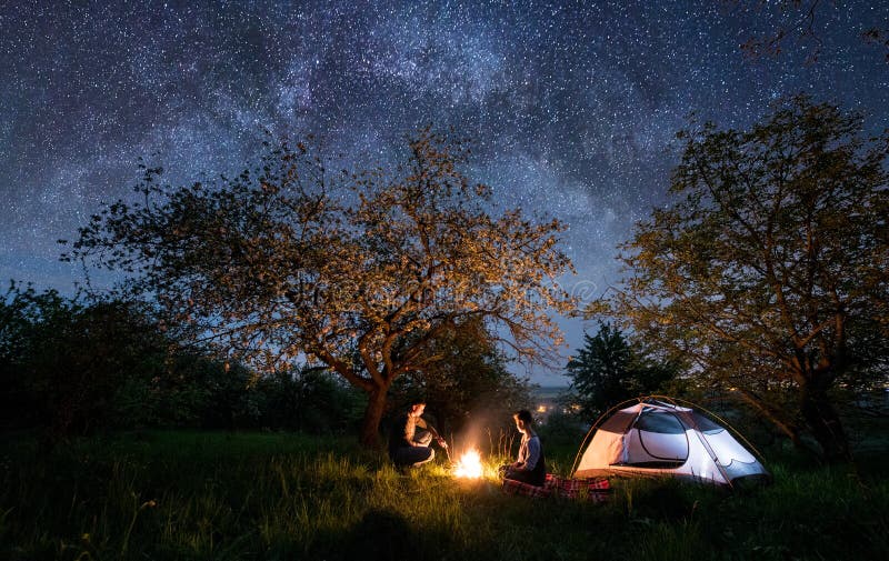 Couple Tourists Sitting at a Campfire Near Tent Under Trees and Night ...