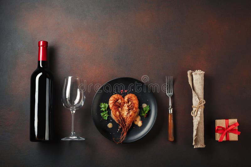 Romantic dinner with heart-shaped shrimps and wine on a brown background